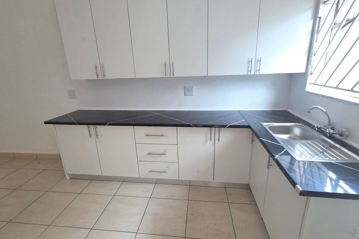 A functional kitchen featuring white built-in cabinetry, dark marble-effect laminate countertops, a stainless steel sink, and tiled flooring.