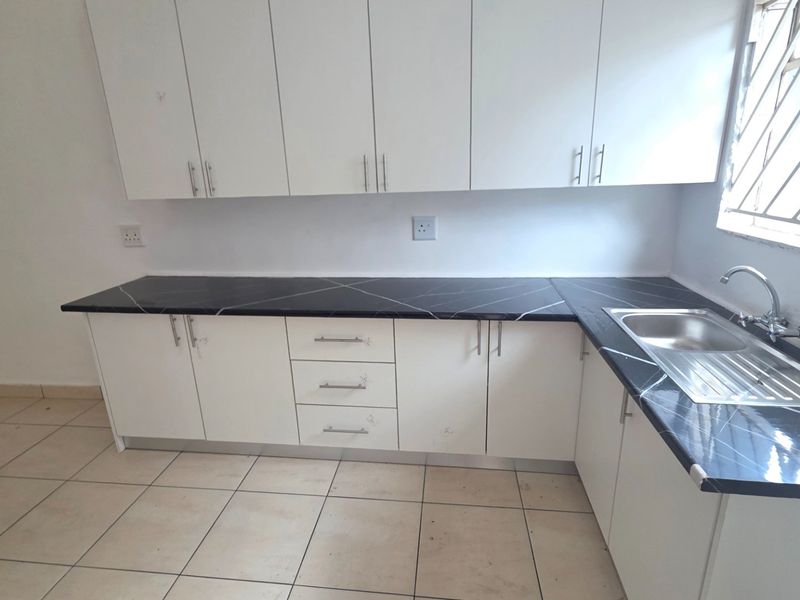 A functional kitchen featuring white built-in cabinetry, dark marble-effect laminate countertops, a stainless steel sink, and tiled flooring.