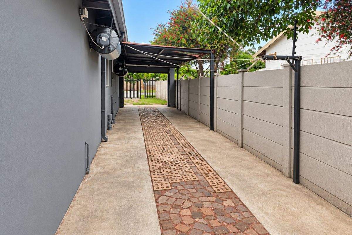A paved side driveway and rear access area featuring a covered carport, concrete boundary walling, and an external geyser installation.