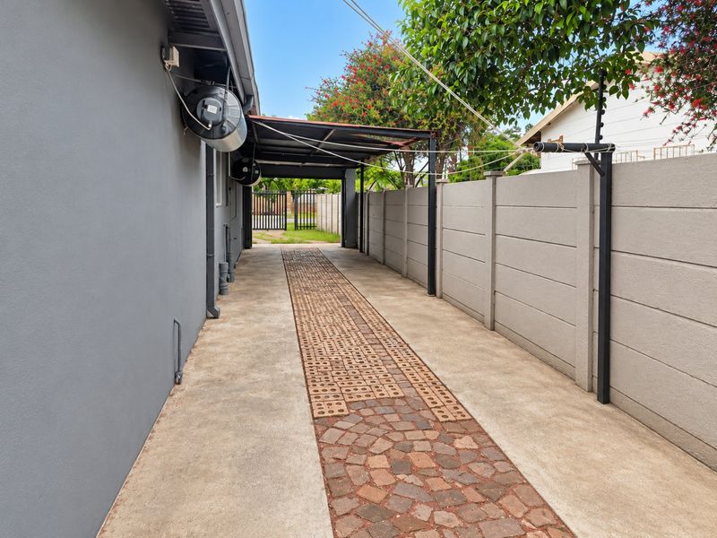 A paved side driveway and rear access area featuring a covered carport, concrete boundary walling, and an external geyser installation.