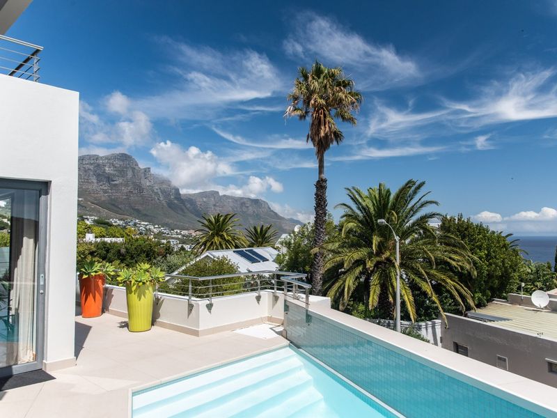 A modern elevated pool area featuring a glass balustrade, tiled patio, and stunning mountain and ocean views.