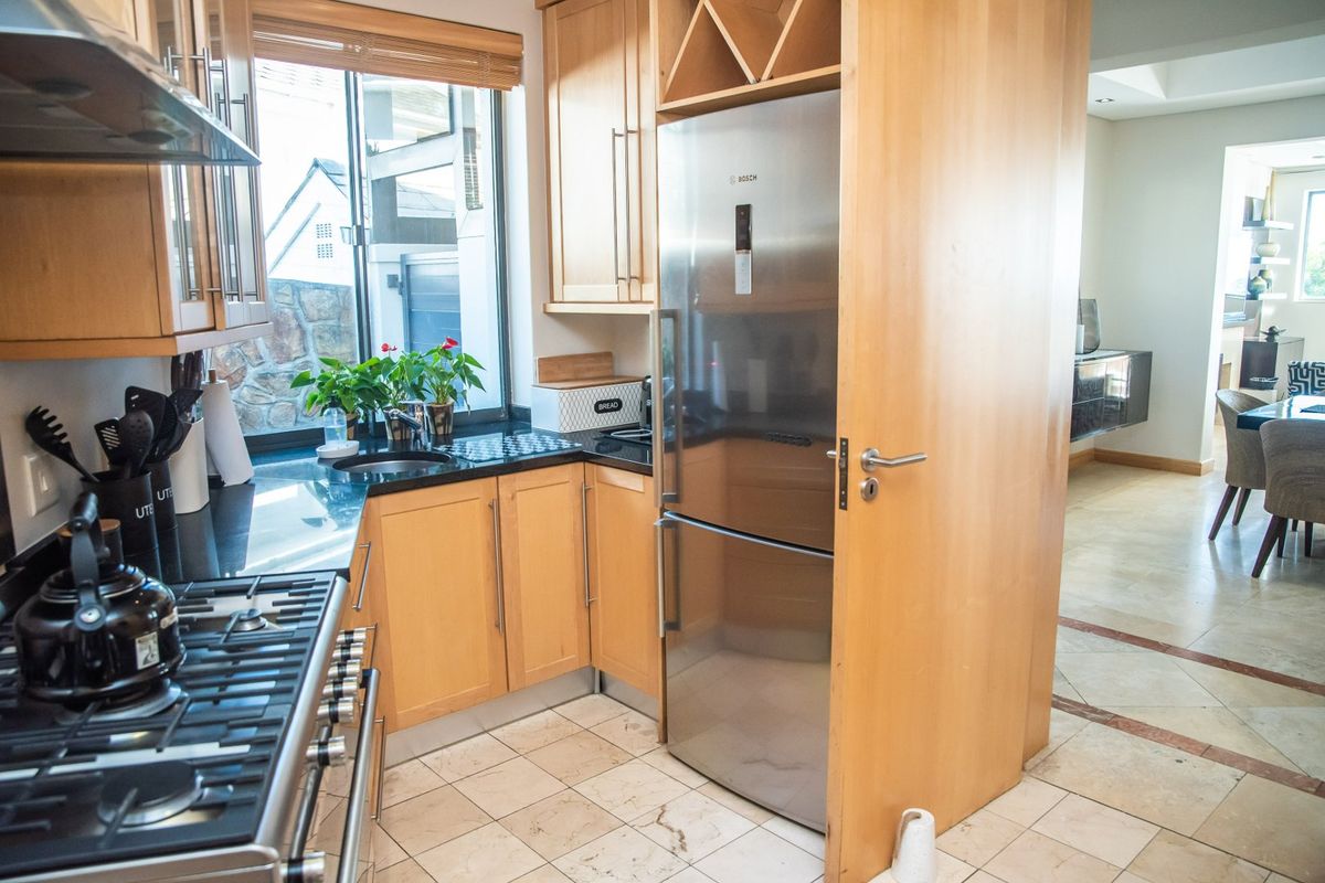 A functional kitchen featuring light wood cabinetry, granite countertops, a gas hob with extractor, and integrated appliances, opening into the main living area.
