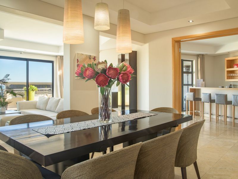 Spacious open-plan dining area featuring stone flooring, modern pendant lighting, and seamless flow to an adjacent bar area and outdoor patio.