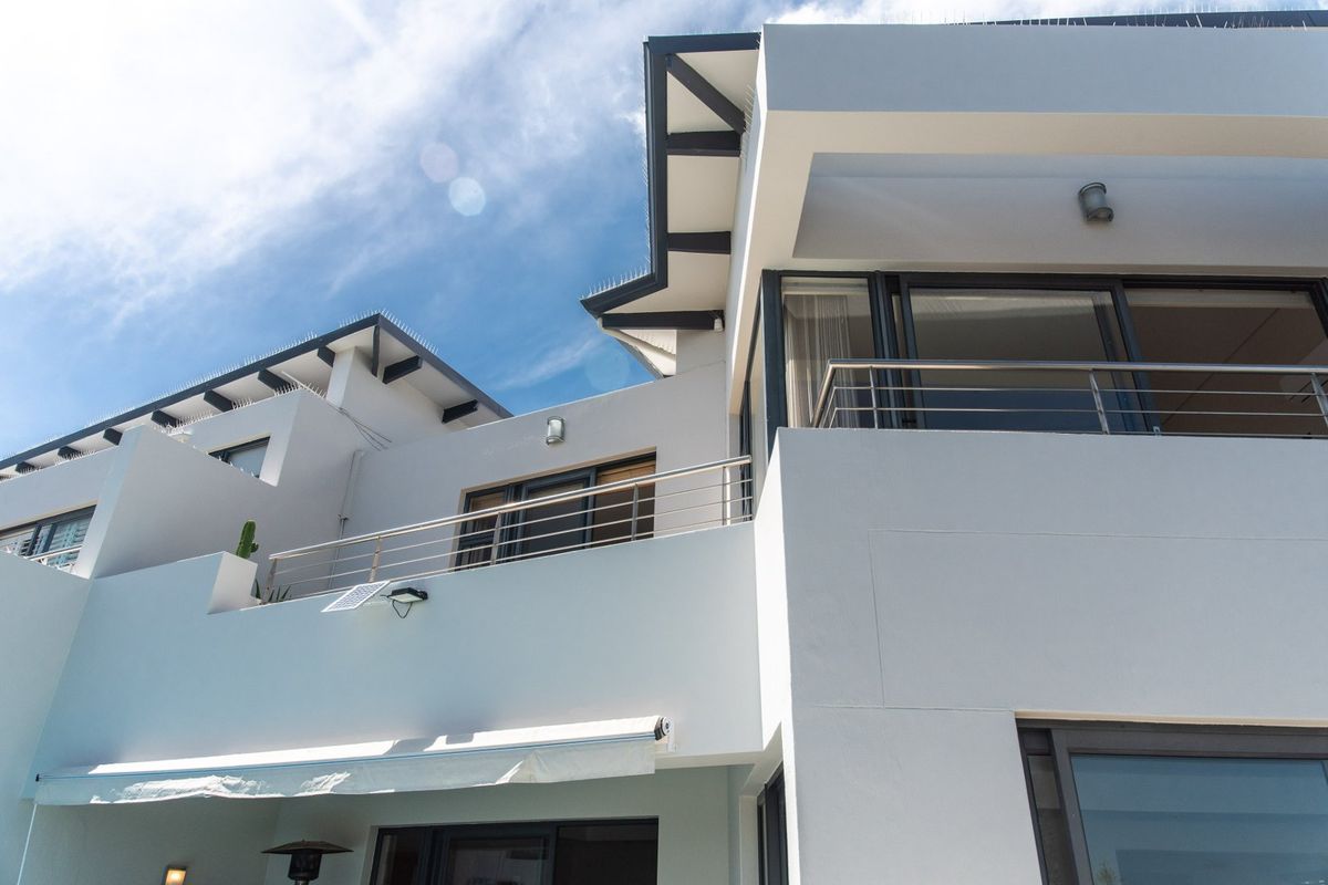 A modern multi-level exterior rear facade featuring balconies with stainless steel railings, sliding glass doors, and a retractable awning.