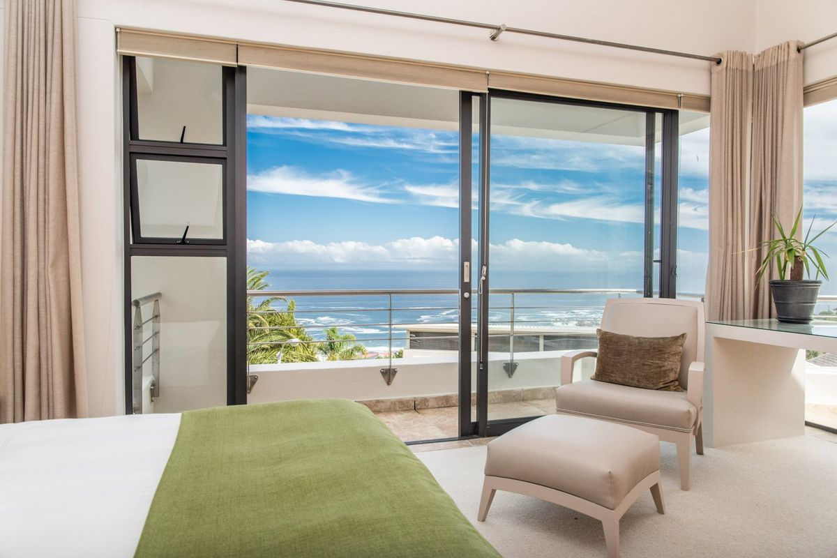 A bright bedroom featuring large sliding glass doors that open onto a private balcony with expansive ocean views.