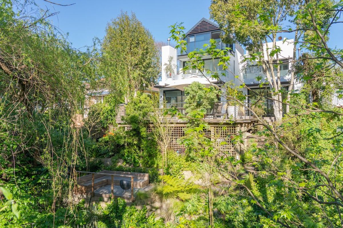 A multi-level rear exterior view of the house featuring extensive timber decking, landscaped gardens, and large glass doors opening onto balconies.