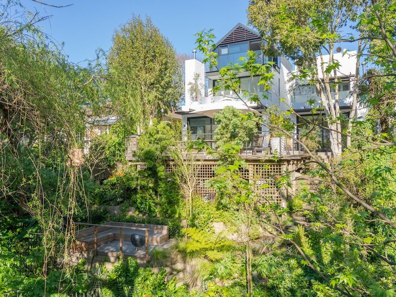 A multi-level rear exterior view of the house featuring extensive timber decking, landscaped gardens, and large glass doors opening onto balconies.