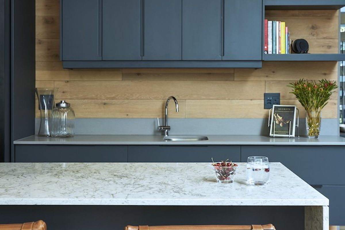 Modern kitchen featuring dark matte cabinetry, timber wall paneling, stone countertops, and a functional island with integrated seating.