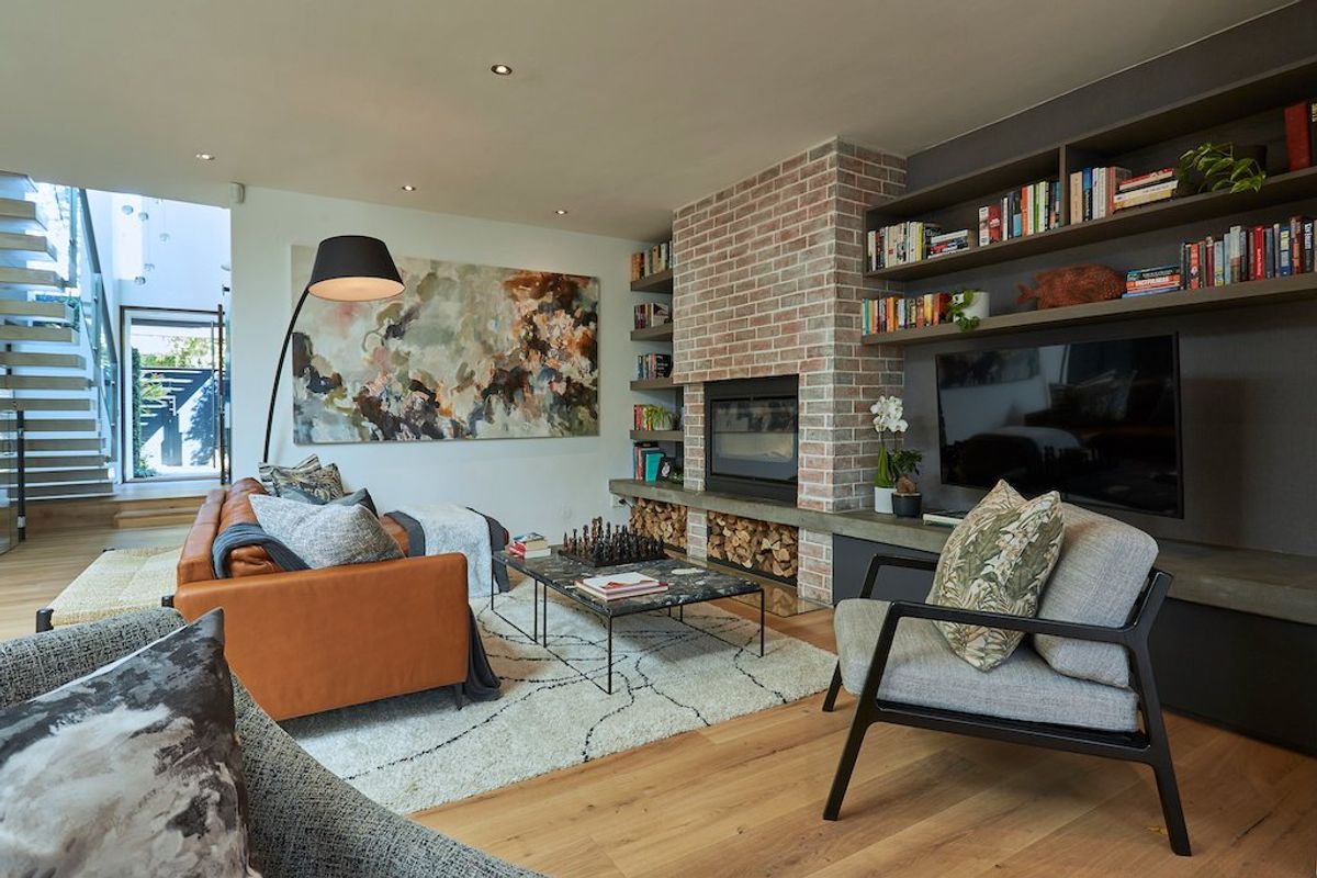 A modern living room featuring a brick fireplace, built-in shelving, and hardwood flooring, with an open staircase leading to the upper level.