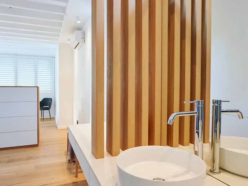Modern bathroom featuring a vessel sink on a stone vanity, accented by a stylish timber slat divider and light timber flooring.