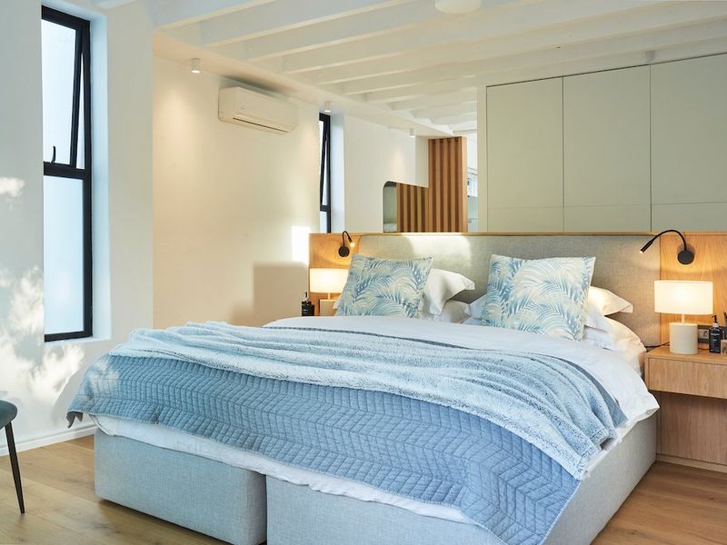 Modern bedroom featuring timber flooring, exposed ceiling beams, built-in cabinetry, and a split-system air conditioning unit.