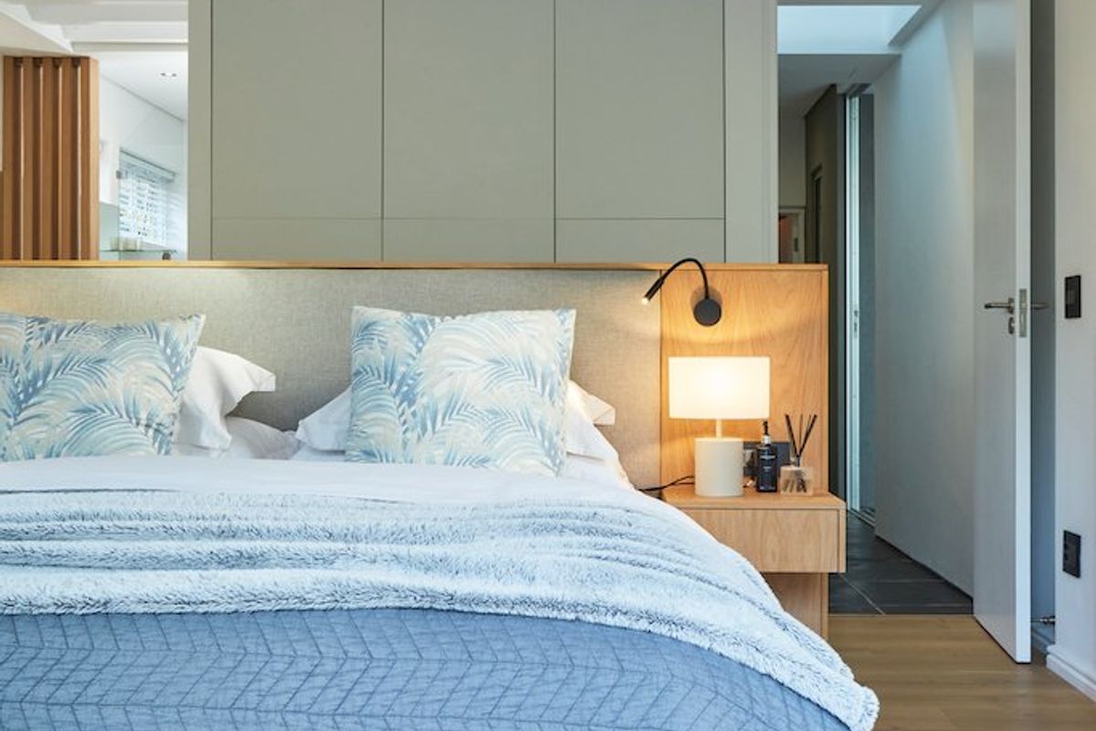 A modern, well-appointed bedroom featuring light timber flooring, built-in cabinetry, and an integrated headboard with warm accent lighting.