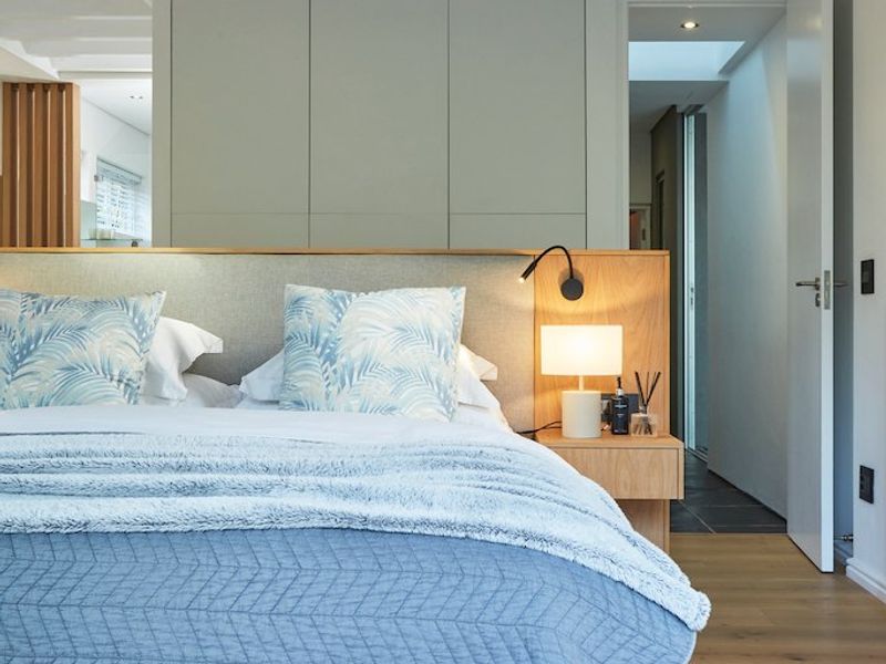 A modern, well-appointed bedroom featuring light timber flooring, built-in cabinetry, and an integrated headboard with warm accent lighting.