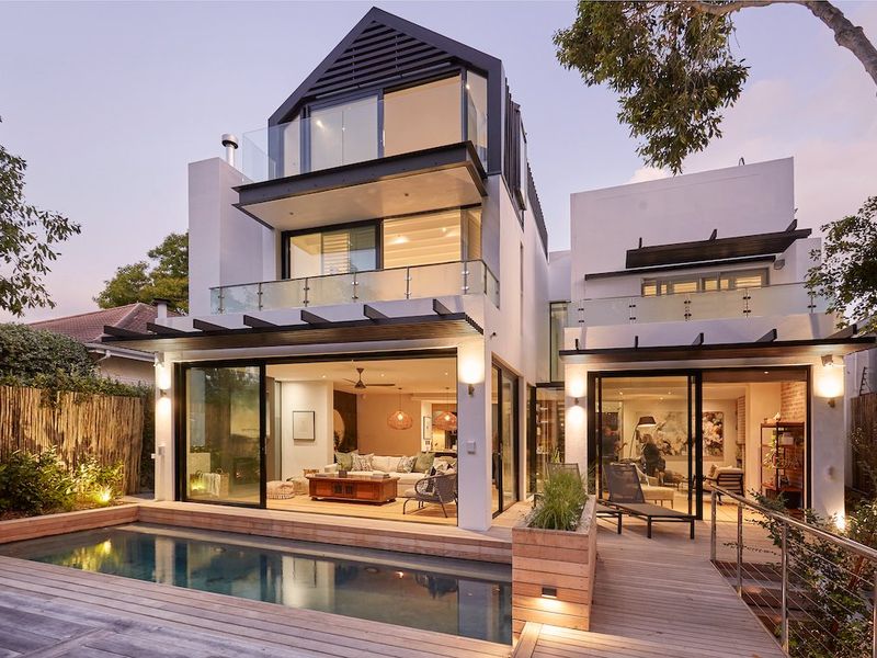 Modern multi-level residence featuring a rear timber deck, swimming pool, and expansive glass sliding doors connecting indoor and outdoor living spaces.