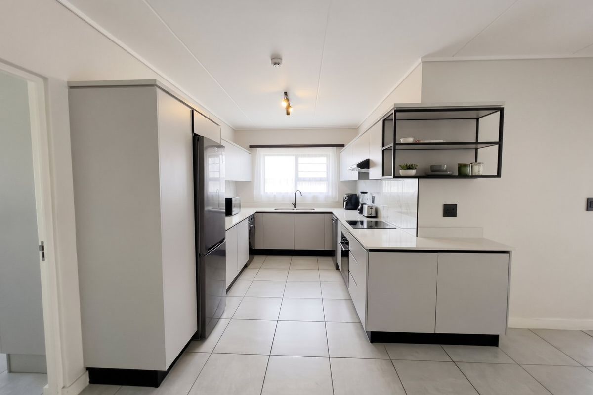 Modern, well-maintained kitchen featuring sleek cabinetry, stone countertops, integrated appliances, and neutral tiled flooring in a clean, functional layout.