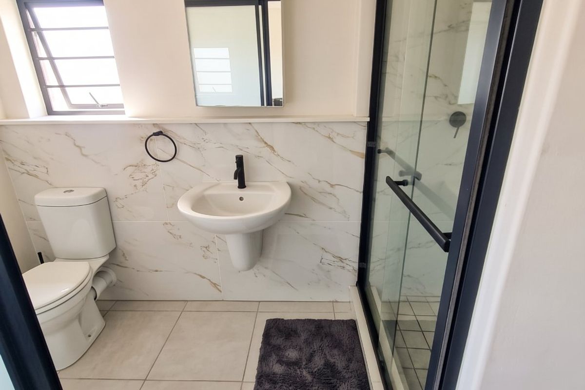 Modern bathroom featuring a pedestal sink, toilet, and a walk-in shower with a sleek black frame and marble-look wall tiling.