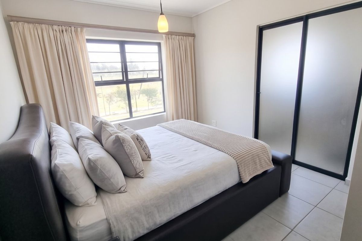 A well-maintained bedroom featuring neutral tiled flooring, a modern sliding door wardrobe, and a large window allowing for natural light.