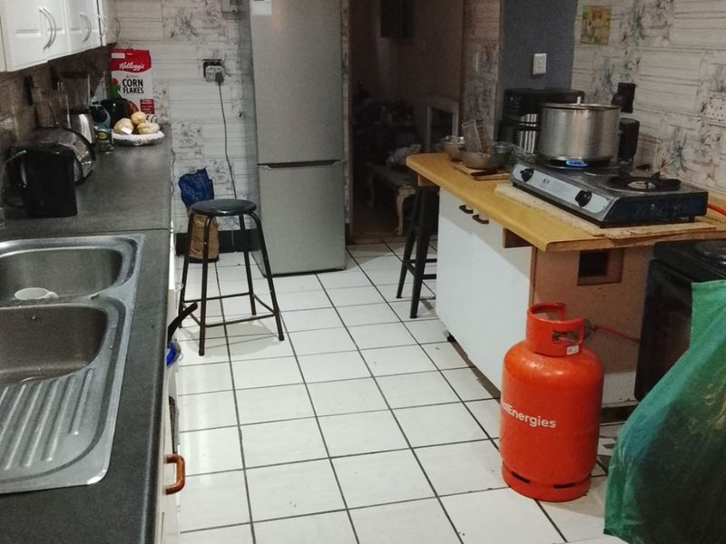 A functional kitchen featuring double bowl sink, laminate countertops, and tiled flooring, currently requiring cosmetic updates to modernize the space.