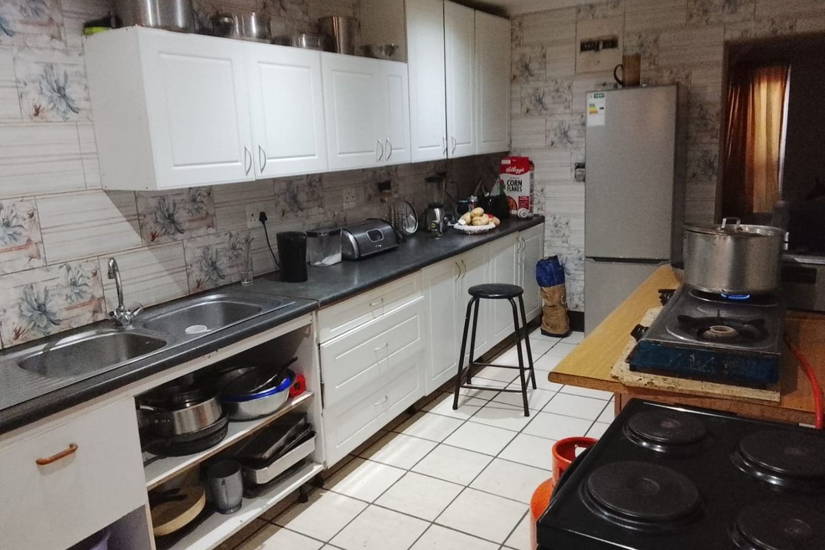 A functional kitchen featuring white cabinetry, laminate countertops, a double stainless steel sink, and ceramic floor tiles with patterned wall tiling.