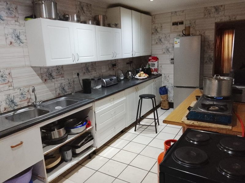 A functional kitchen featuring white cabinetry, laminate countertops, a double stainless steel sink, and ceramic floor tiles with patterned wall tiling.