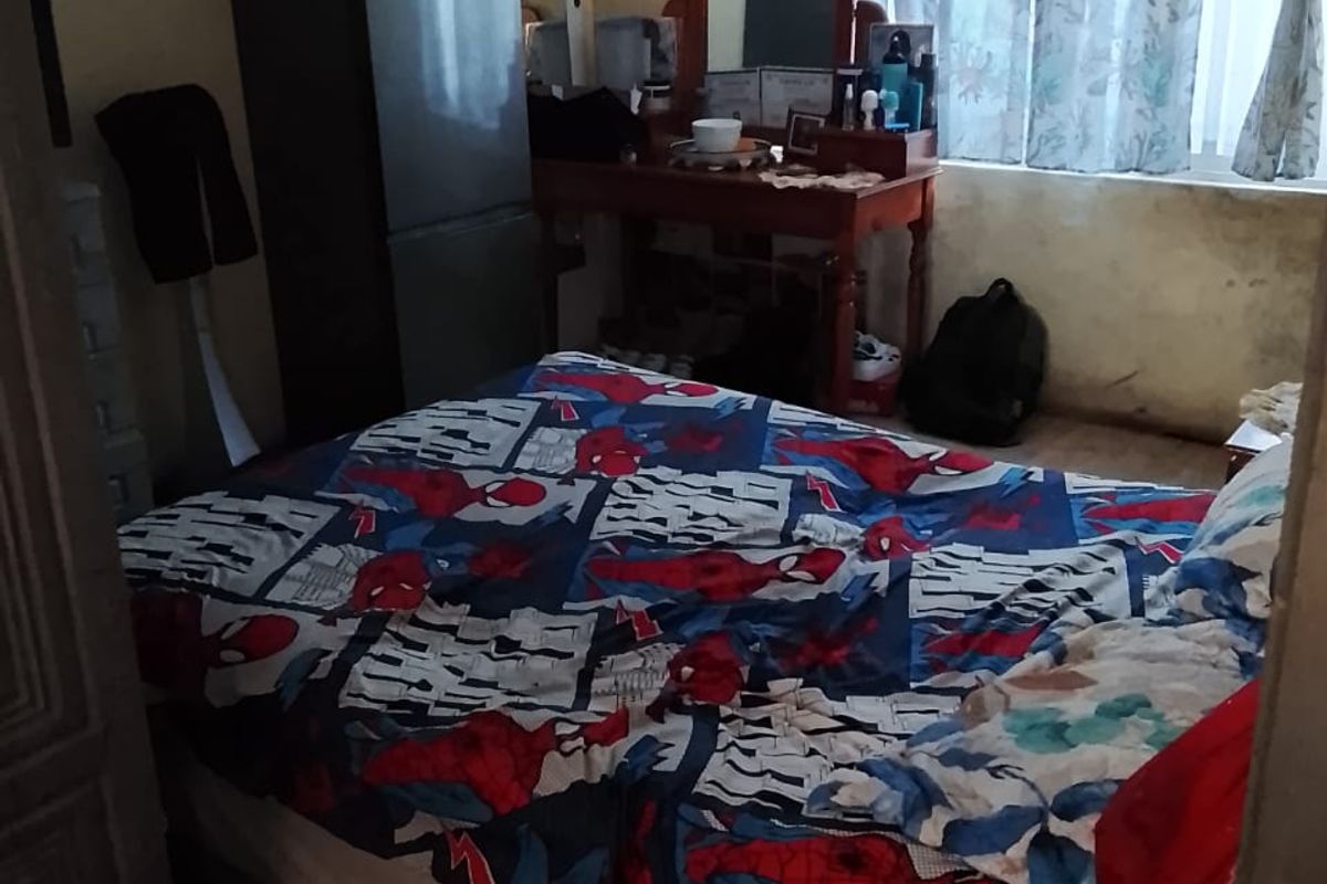 A bedroom featuring a window with curtains and visible wear on the wall surfaces, requiring cosmetic updates to improve the overall condition.