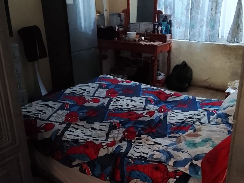 A bedroom featuring a window with curtains and visible wear on the wall surfaces, requiring cosmetic updates to improve the overall condition.
