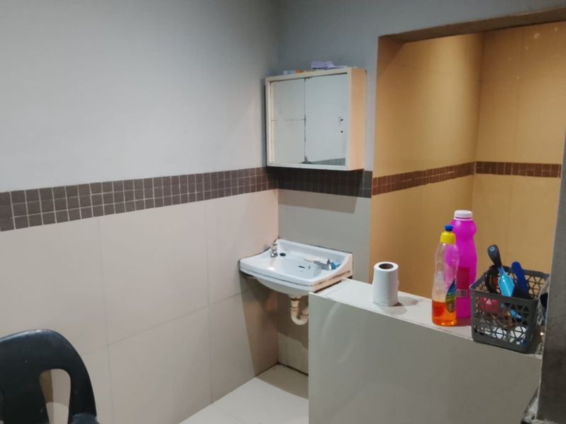 A functional bathroom space featuring a wall-mounted basin, tiled splashback, and a built-in medicine cabinet, requiring cosmetic updates to improve its overall condition.