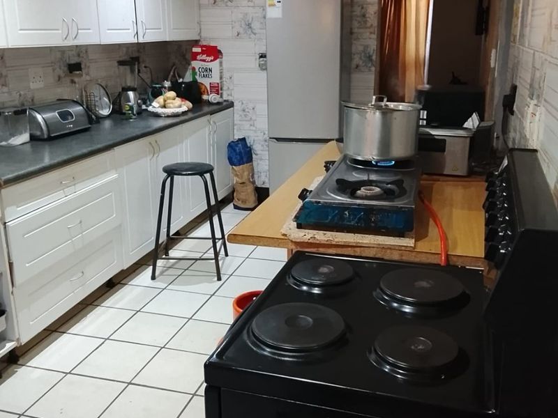 A functional kitchen featuring white cabinetry, dark countertops, and tiled flooring, currently equipped with both electric and gas cooking appliances.