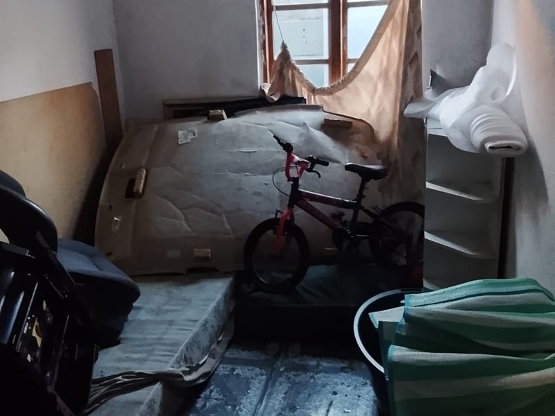 A small bedroom space featuring tiled flooring and a timber-framed window, currently in need of significant cosmetic renovation and repair.