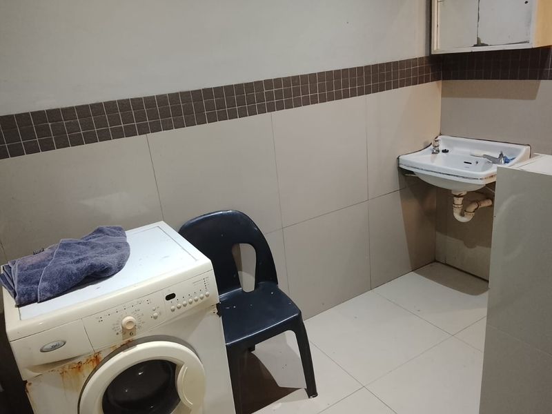 Functional laundry area featuring tiled walls and flooring with a wall-mounted basin and dedicated space for laundry appliances.
