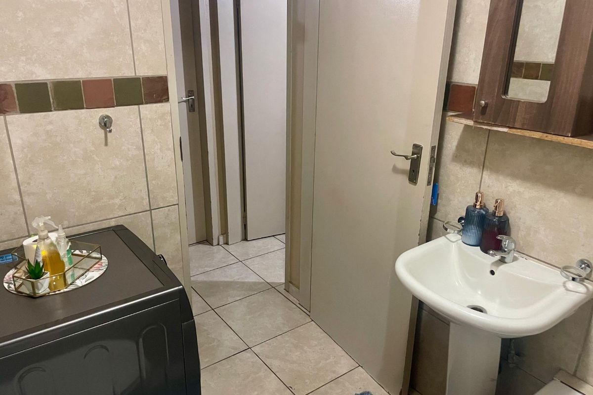 A functional bathroom featuring a pedestal sink, tiled walls with decorative accents, and a wall-mounted mirror cabinet, providing essential utility in a compact layout.