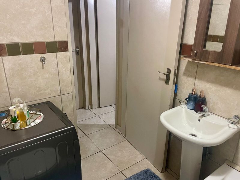 A functional bathroom featuring a pedestal sink, tiled walls with decorative accents, and a wall-mounted mirror cabinet, providing essential utility in a compact layout.