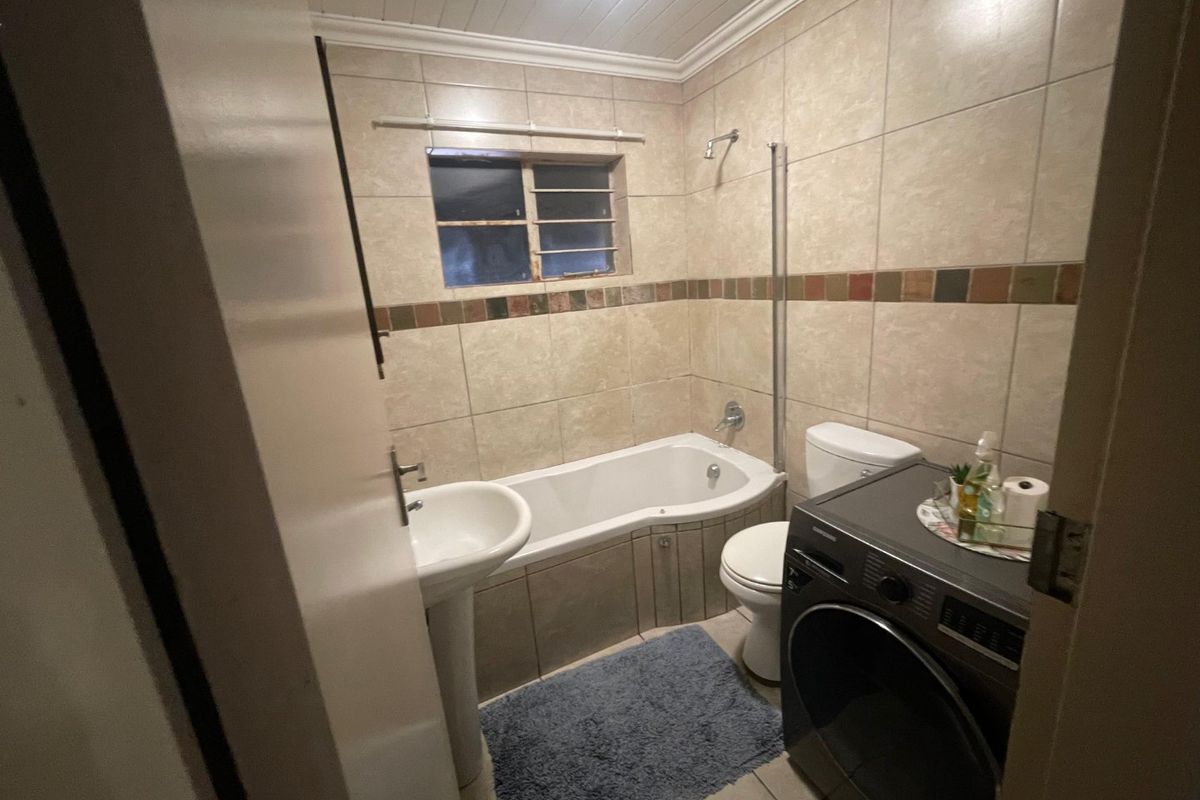 A functional bathroom featuring a pedestal basin, built-in bathtub with shower head, and toilet, finished with neutral wall tiles and a tiled floor.
