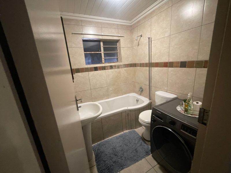 A functional bathroom featuring a pedestal basin, built-in bathtub with shower head, and toilet, finished with neutral wall tiles and a tiled floor.