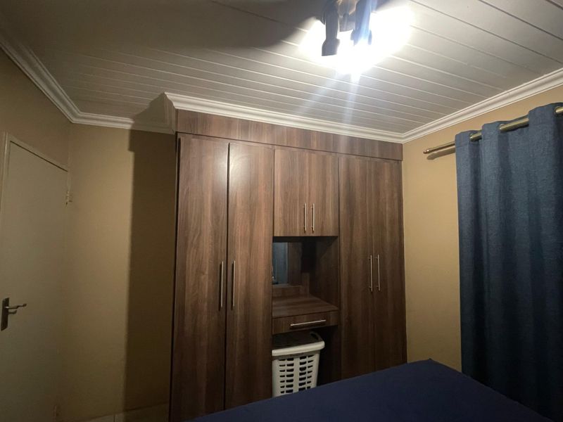 A bedroom featuring dark wood built-in cupboards with an integrated vanity unit and a white tongue and groove ceiling.