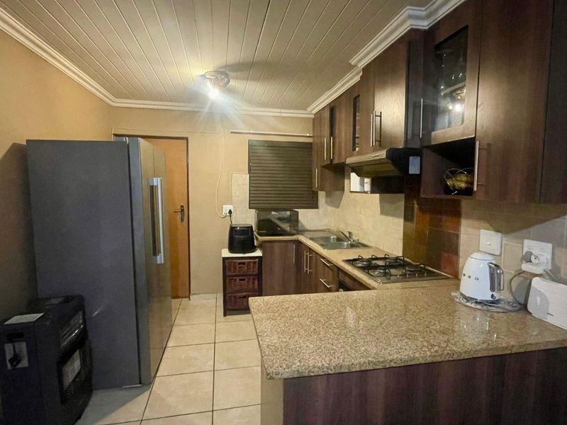 Functional kitchen featuring granite countertops, gas hob, extractor fan, and ample built-in cabinetry with tiled flooring and a timber panelled ceiling.
