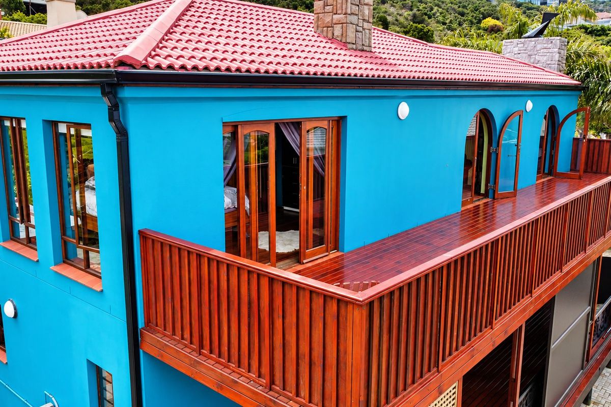 An elevated view of the rear exterior featuring a vibrant blue facade, a terracotta tiled roof, and a spacious timber balcony with wooden balustrades.