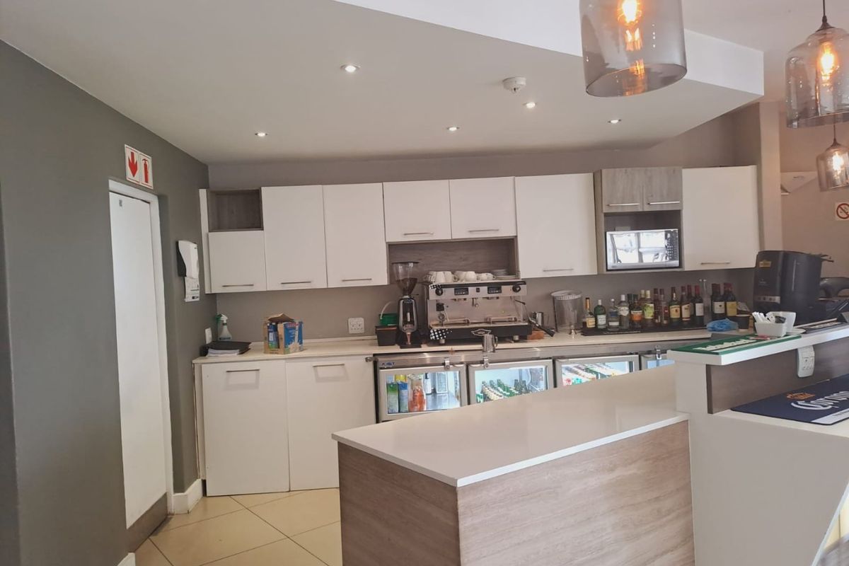 A modern kitchen area featuring white cabinetry, stone countertops, under-counter refrigeration, and stylish pendant lighting, suitable for a bar or service space.