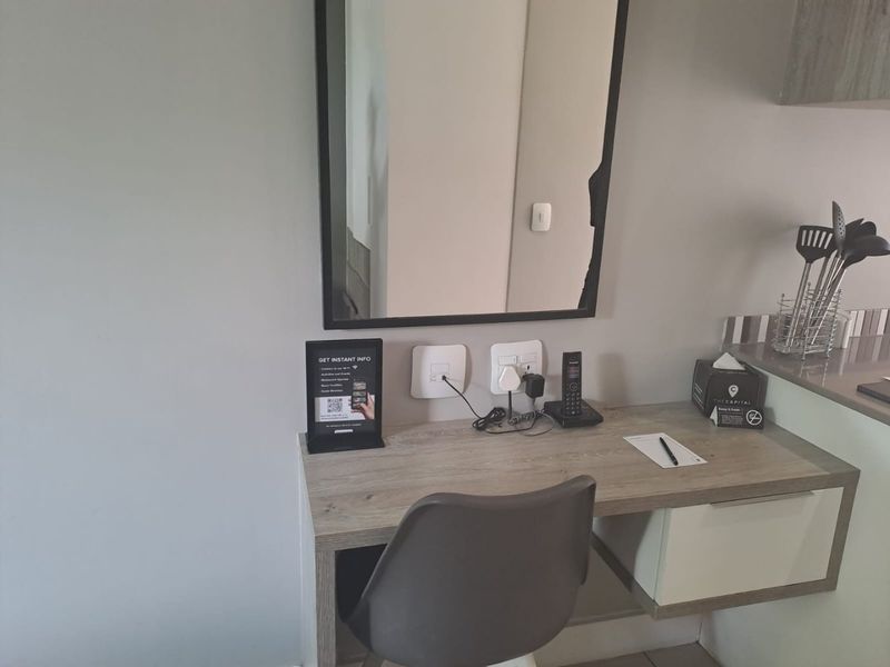 A functional bedroom workspace featuring a built-in desk, wall-mounted mirror, and integrated electrical outlets for convenience.