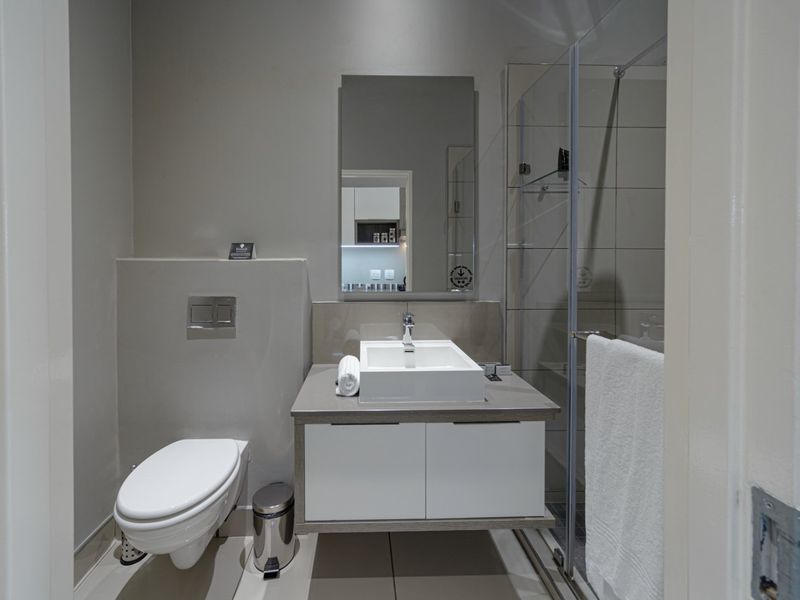 Modern bathroom featuring a wall-hung toilet with concealed cistern, a sleek vanity with vessel sink, and a glass-enclosed shower.