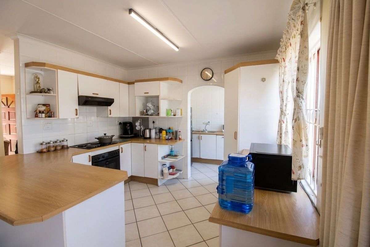 A functional kitchen featuring white cabinetry, laminate countertops, tiled flooring, and a separate scullery area with a sink.