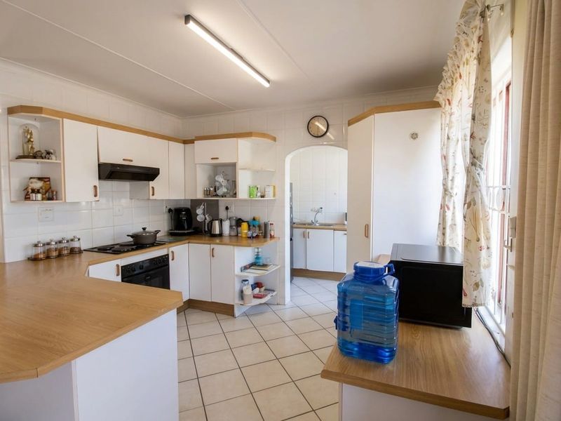 A functional kitchen featuring white cabinetry, laminate countertops, tiled flooring, and a separate scullery area with a sink.
