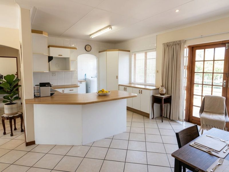 Open plan kitchen and dining area featuring tiled flooring, ample built-in cabinetry, laminate countertops, and direct access to the outdoors through wooden french doors.