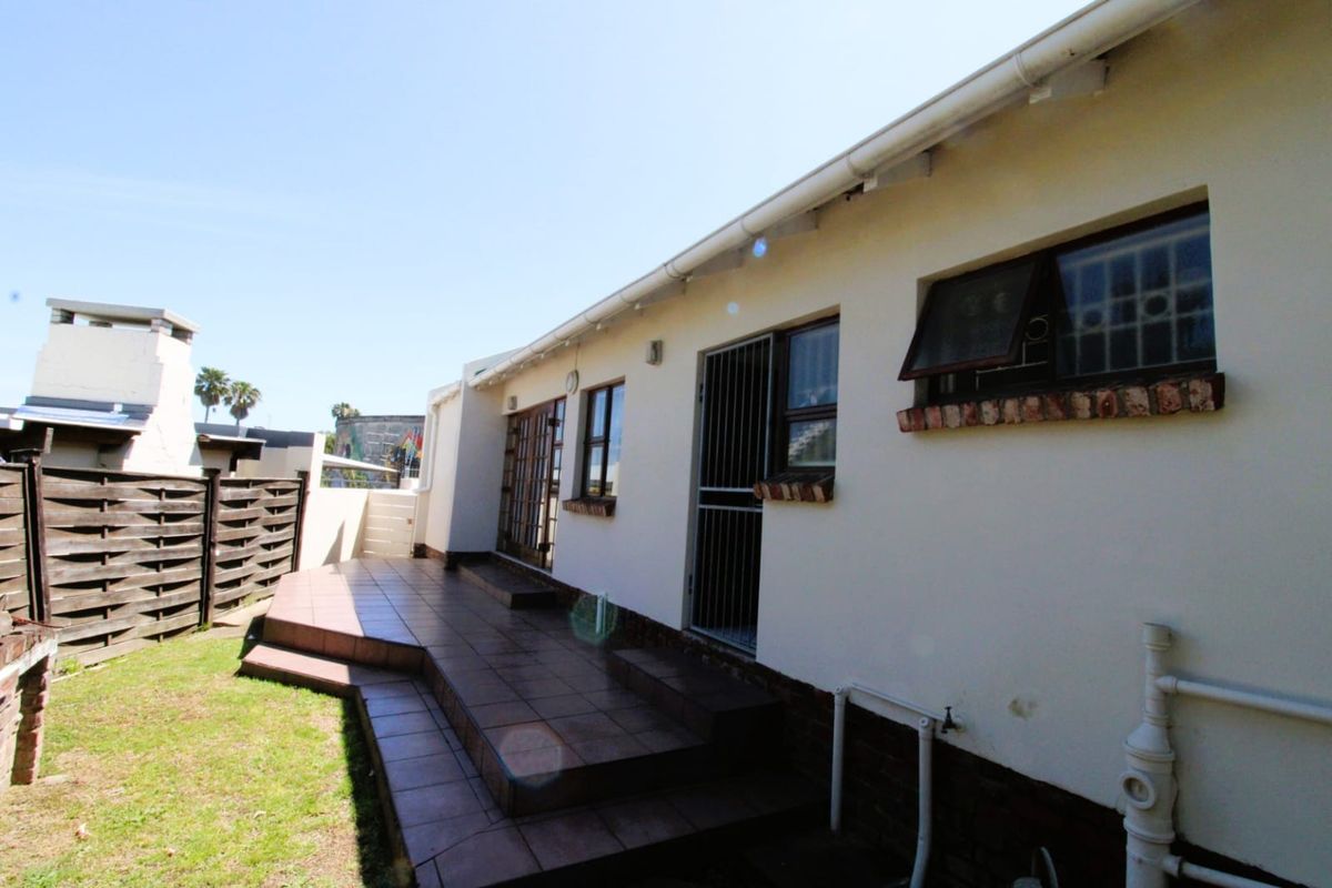Rear exterior view of the townhouse featuring a tiled patio area, security gates, and a small garden space with timber fencing.