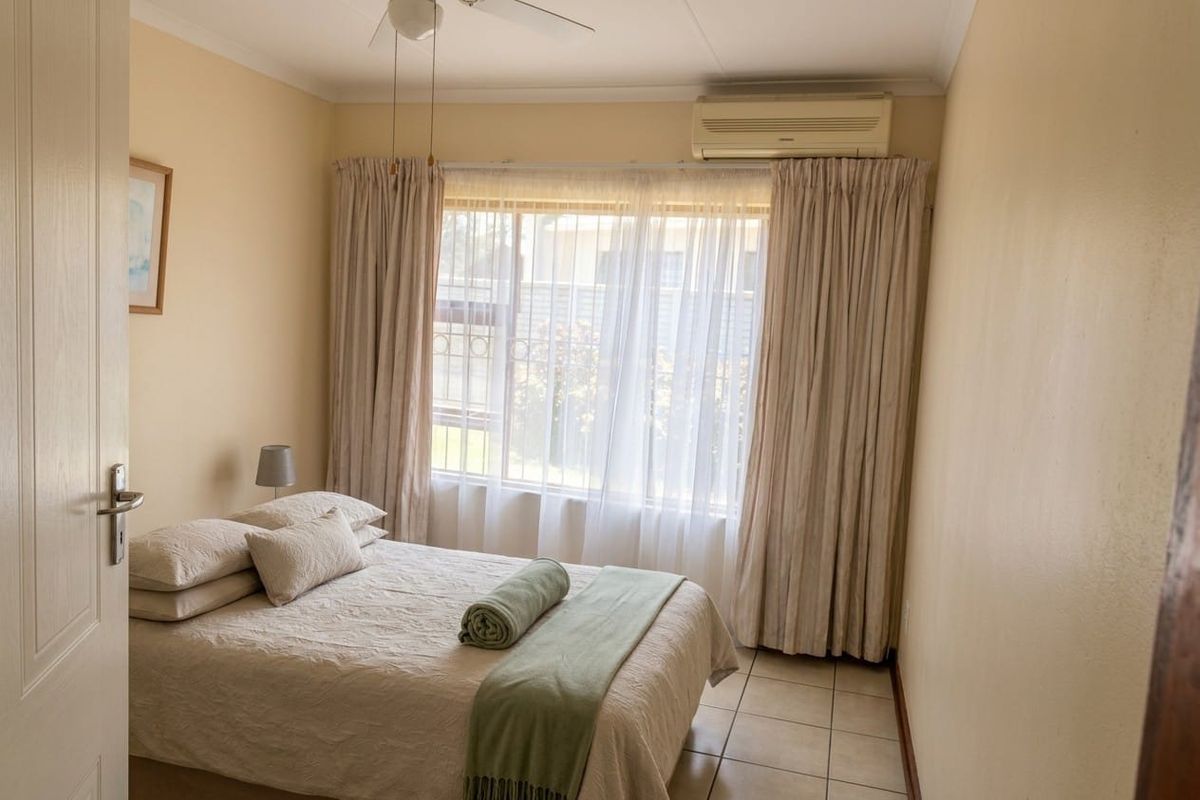 A cozy bedroom featuring tiled flooring, a ceiling fan, and a wall-mounted split-system air conditioner for climate control.