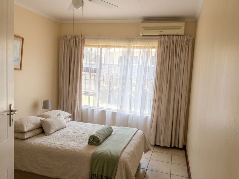 A cozy bedroom featuring tiled flooring, a ceiling fan, and a wall-mounted split-system air conditioner for climate control.