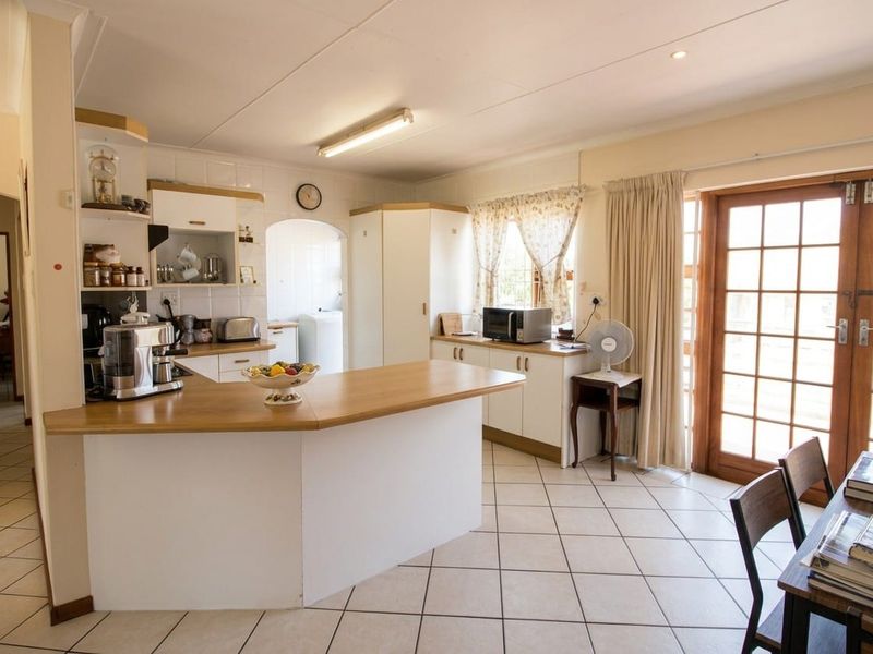 A functional kitchen featuring tiled flooring, ample cabinetry, laminate countertops, and direct access to the outdoors through wooden french doors.