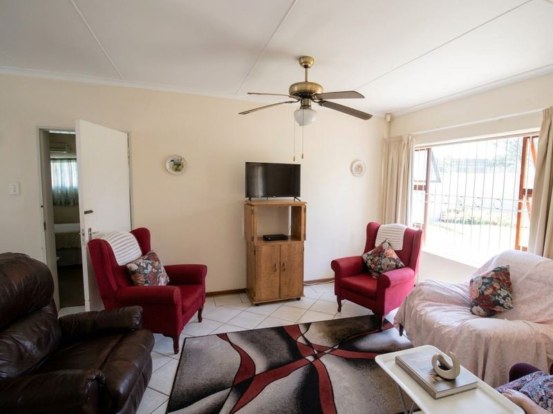 A comfortable living room featuring tiled flooring, a ceiling fan, and large windows with security bars, offering a functional and well-lit space.