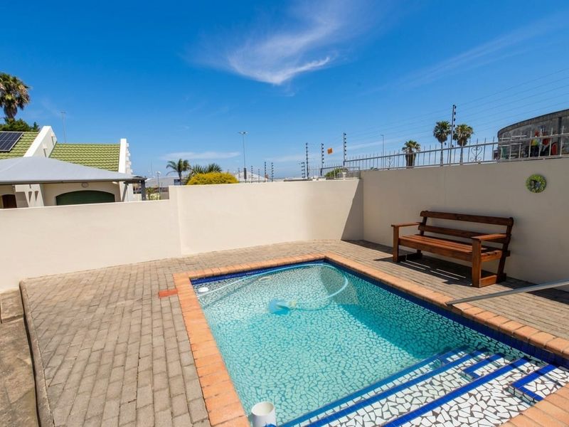 A private outdoor pool area featuring a paved patio, boundary wall with electric fencing, and a compact swimming pool.