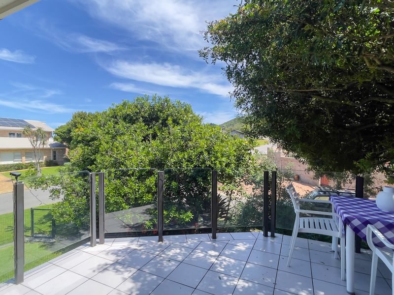 An elevated balcony featuring a modern glass balustrade and tiled flooring, offering a pleasant outdoor space with views of the surrounding neighborhood.